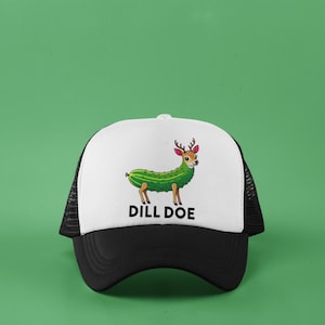 May include: A black and white trucker hat with a white front panel featuring a cartoon illustration of a deer with a pickle body. The text "DILL DOE" is printed below the image. The hat has a curved brim and a mesh back.
