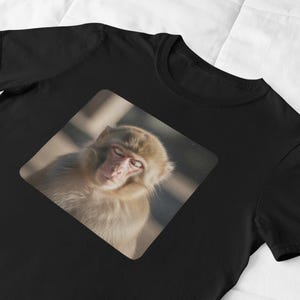 May include: Black t-shirt featuring a square image of a sleeping monkey. The monkey has light brown fur and is resting with its eyes closed. The shirt is made of a soft material and is suitable for casual wear.