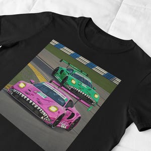 May include: A black t-shirt with a graphic print of two race cars on a track. The cars are pink and green with a toothy design on the front.