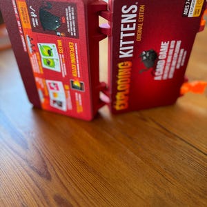 Custom 3D-printed storage box for Exploding Kittens. Holds cards securely with a built-in divider, doubles as a deck and discard holder. UV-printed artwork ensures crisp, vibrant designs. Perfect for organising and upgrading your game night setup.