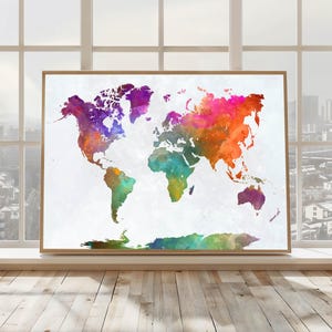 May include: A framed watercolor world map print. The map features a vibrant color palette of purple, orange, green, and blue hues. The artwork is displayed in a light brown wooden frame, set against a white background.