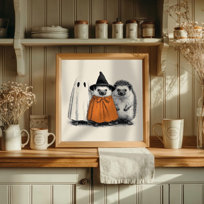 May include: A framed Halloween-themed illustration featuring a ghost, a hedgehog in an orange cape and witch hat, and another hedgehog. The artwork is in black and white with orange accents, perfect for seasonal decor.