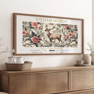 May include: A framed poster with a vintage aesthetic featuring a deer standing in a field of flowers. The poster is titled "William Morris Cotton Prints Exhibition" and includes details about the exhibition, including the dates, location, and admission price.