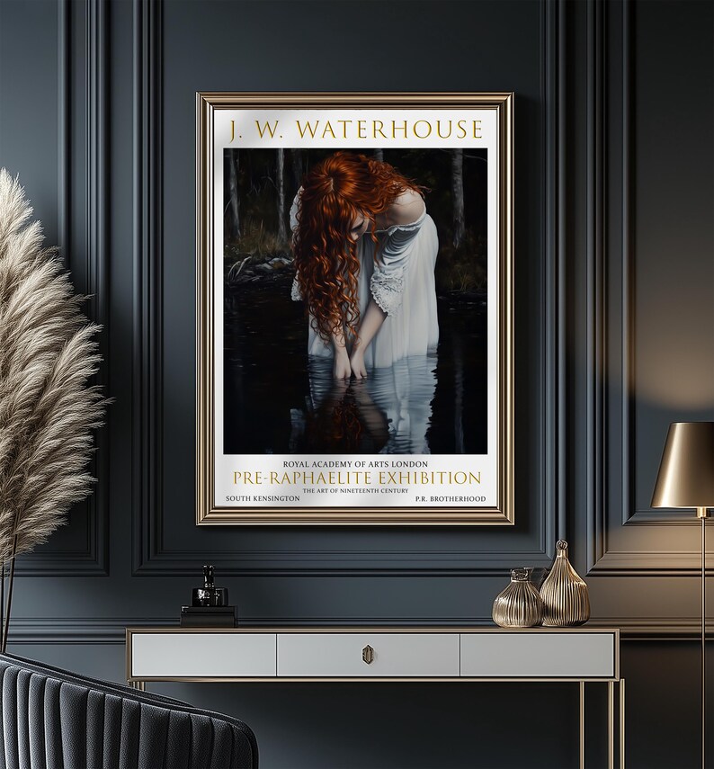 May include: A framed art print of a J.W. Waterhouse painting. The image shows a woman with red hair in a white dress, standing in water. The gold frame surrounds the artwork, with text for a Pre-Raphaelite exhibition.