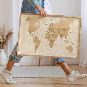 May include: A framed world map with a vintage design. The map shows continents and countries in brown and beige tones. The wooden frame gives it a classic look. This map is a decorative item, ideal for display in a home or office setting.