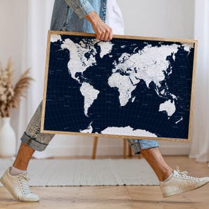 May include: A framed world map with a navy blue background and white continents. The map is in a light brown wooden frame. The map shows the world's countries and oceans.