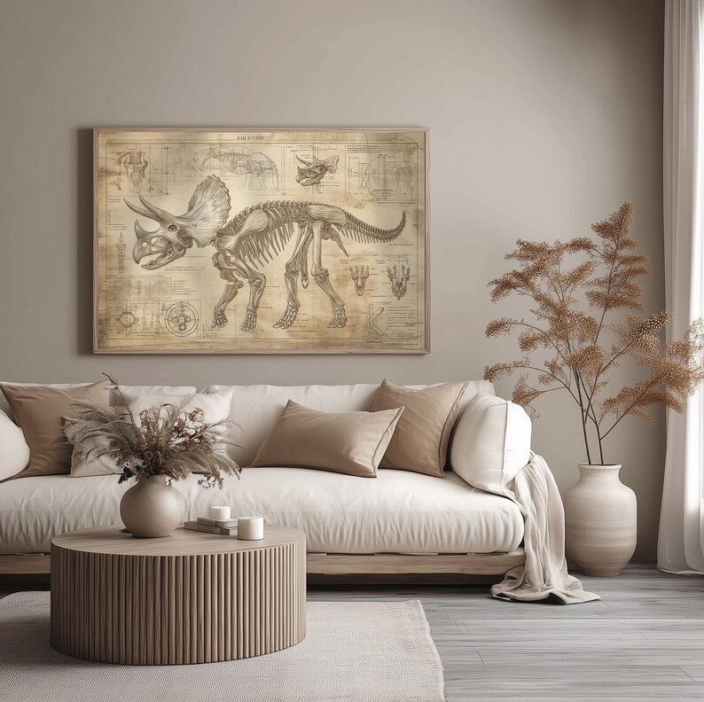 May include: A vintage-style illustration of a Triceratops skeleton on a beige background. The illustration is framed and hanging on a wall above a white couch with beige throw pillows. A potted plant with brown branches is on the right side of the image.