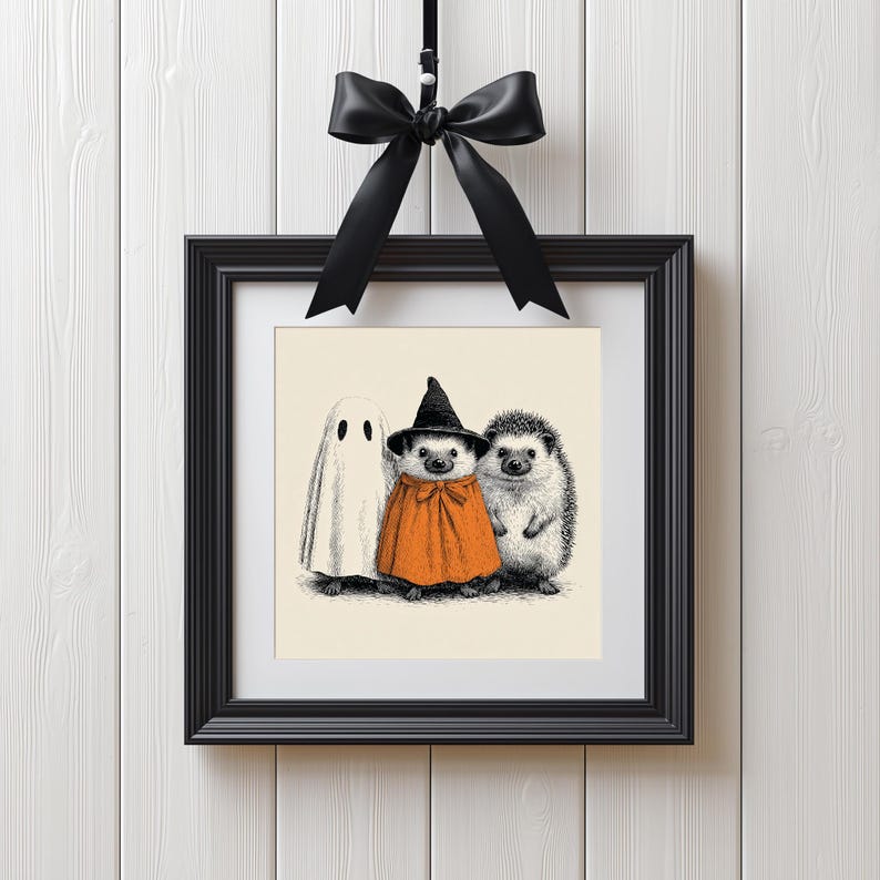 May include: A framed Halloween-themed print featuring a ghost and two hedgehogs. One hedgehog is dressed as a witch in an orange cape and black hat. The other hedgehog is in its natural state. The print is in a black frame and is suspended by a black ribbon.