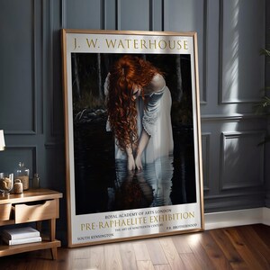 May include: A framed art print of a J.W. Waterhouse painting. The image shows a woman with flowing red hair in a white dress, standing in water. The print includes text: "PRE-RAPHAELITE EXHIBITION" and "ROYAL ACADEMY OF ARTS LONDON".