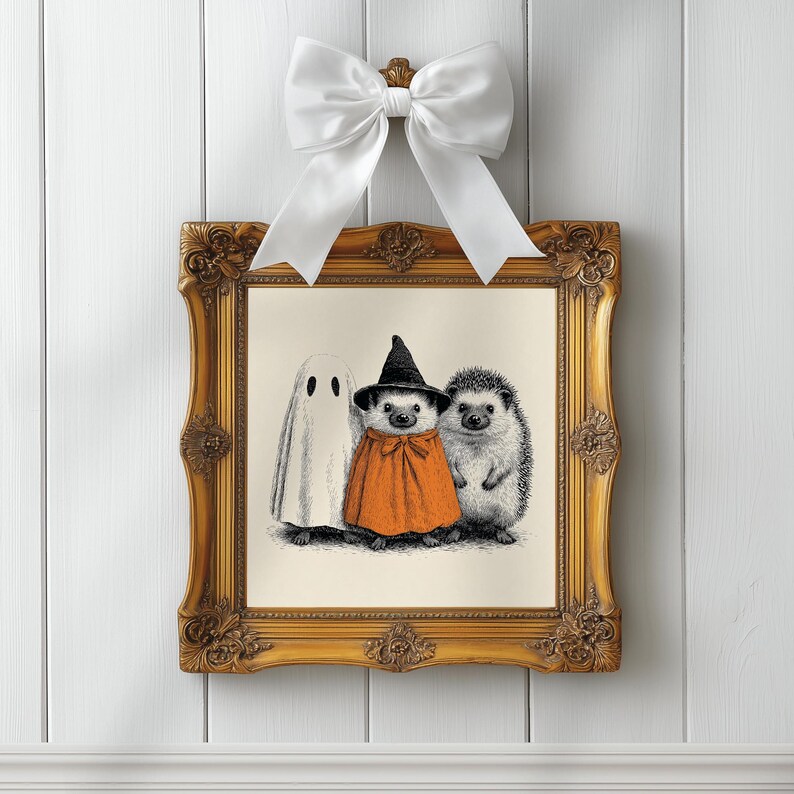 May include: A framed Halloween-themed print featuring a ghost, a hedgehog in an orange cape and witch hat, and another hedgehog. The ornate gold frame is topped with a white bow, creating a festive and whimsical display.