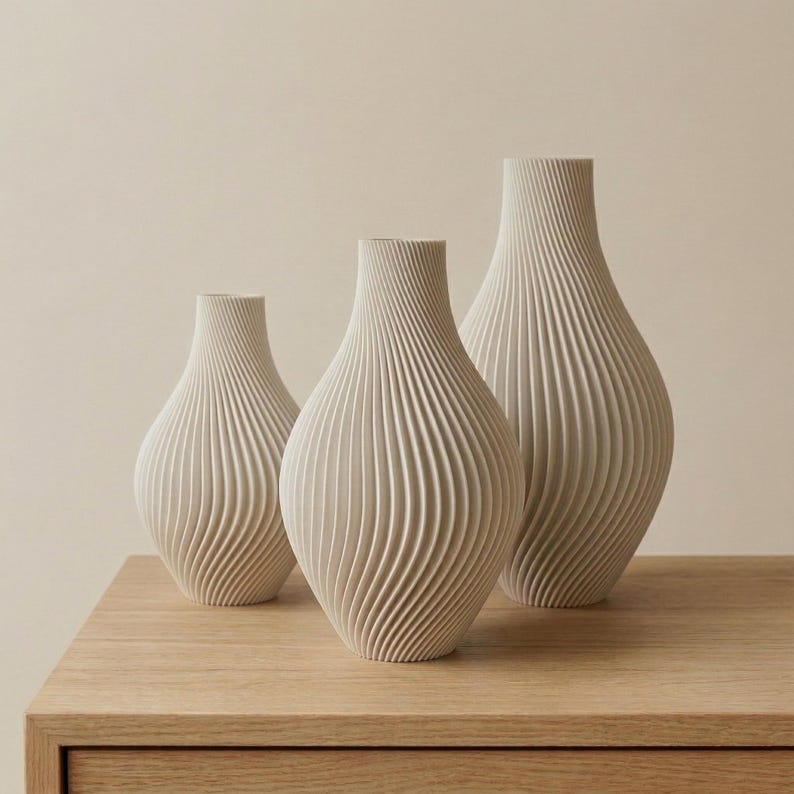 Może przedstawiać: Trzy beżowe ceramiczne wazony o żebrowanym, spiralnym wzorze. Wazony mają r&oacute;żne wysokości i stoją na jasnej drewnianej powierzchni. Tło jest jednolite, neutralne.