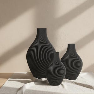 Może przedstawiać: Zestaw trzech ceramicznych kubk&oacute;w z nakrapianym, matowym wykończeniem. Kubki są w odcieniach kremu, jasnoszarym i ciemnoszarym. Każdy kubek ma prosty, minimalistyczny design, idealny do kawy lub herbaty.