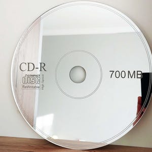 May include: A silver CD-R disc with the text "CD-R" and "700 MB" printed on it. The disc is labeled as a "Compact Disc" and is "ReWritable" and "High Speed".