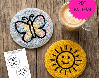 May include: Two handmade, round coasters. One features a butterfly design with pastel colours and black outline. The other is yellow with a smiling sun design. A cup of coffee and a template with butterfly and sun designs are also present.