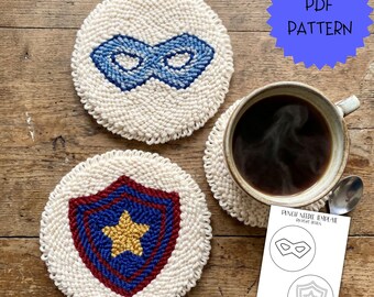 May include: Three handmade, round coasters with superhero designs. One features a blue mask, another a shield with a gold star, and the third is under a coffee cup. The coasters are made with a cream-coloured yarn.