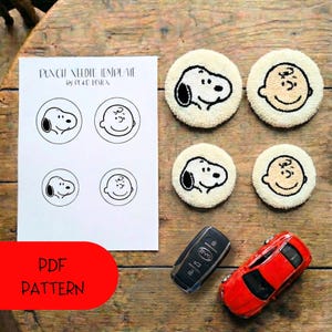 Könnte beinhalten: Auf einem Holztisch liegen eine Punch-Needle-Vorlage mit Snoopy- und Charlie-Brown-Designs sowie vier fertige runde Untersetzer. Ein rotes Spielzeugauto und ein Autoschlüssel sind ebenfalls vorhanden. Die Vorlage lautet "PUNCH NEEDLE TEMPLATE" und "PDF PATTERN."