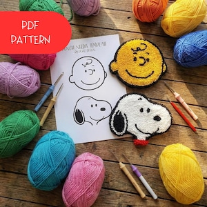 Może przedstawiać: Szablon do haftu igłą z motywami Charlie'ego Browna i Snoopy'ego, otoczony kolorowymi kulkami przędzy i narzędziami do haftu igłą. Tekst "PDF PATTERN" znajduje się w czerwonym owalu. Wzory Snoopy'ego i Charliego Browna wykonane są z żółtej i białej przędzy.