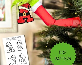 May include: A punch needle pattern PDF template featuring the letters A, B, C, and D styled as Santa Claus suits with hats and belts. A green fuzzy hand holds a finished letter A ornament with a red and white Santa suit design on a tree.