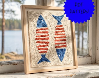 May include: A square punch needle embroidery piece framed in light wood, featuring two stylized fish with blue heads and tails and horizontal orange stripes on a cream-colored background. A blue starburst graphic displays the text PDF PATTERN.