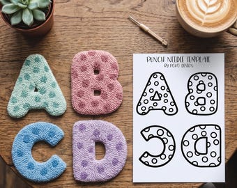May include: Four tufted fabric letters A, B, C, and D in pastel mint, pink, blue, and lavender with polka dot patterns, alongside a white paper sheet titled PUNCH NEEDLE TEMPLATE BY POKO DESIGN featuring black line art outlines of the same letters.