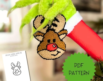 May include: A punch needle reindeer ornament with a brown face, tan antlers, and a bright red nose, held by a fuzzy green hand. A white card displays the text PUNCH NEEDLE TEMPLATE BY PEWD DESIGN, and a green starburst graphic reads PDF PATTERN.
