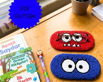 May include: Two oval-shaped punch needle mats, one red and one blue, each featuring large white eyes. The red mat has small white teeth and holds a pair of glasses. A blue star-shaped graphic with the text PDF PATTERN is visible.