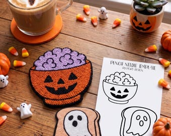 May include: A punch needle project featuring a jack-o'-lantern bowl with purple contents and a ghost on toast, accompanied by a printed template labelled PUNCH NEEDLE TEMPLATE by POKO DESIGN, showcasing line art of the bowl and ghost designs.
