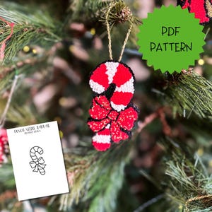 May include: A punch needle ornament shaped like a candy cane with a red and white striped pattern and a red bow, hanging by a gold cord. A white card displays the text PUNCH NEEDLE TEMPLATE BY PEVO DESIGN and a black line drawing of the candy cane.