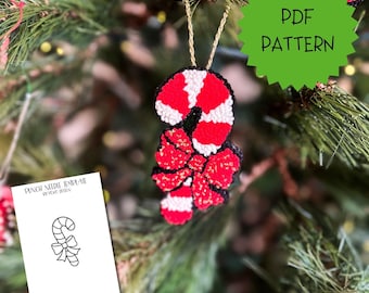 May include: A punch needle ornament shaped like a candy cane with a red and white striped pattern and a red bow, hanging by a gold cord. A white card displays the text PUNCH NEEDLE TEMPLATE BY PEVO DESIGN and a black line drawing of the candy cane.