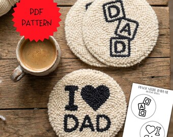 May include: Circular beige coasters with black embroidered text and heart designs. One says "DAD" in blocks, another says "I ❤️ DAD". A red tag reads "PDF PATTERN". A cup of coffee is also visible.