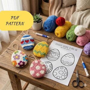 Puede incluir: Una colección de ovillos de lana coloridos, herramientas de punch needle y adornos de huevos de Pascua sobre una mesa de madera. Los adornos presentan varios diseños, incluyendo corazones, flores y lunares. También se ve una hoja con plantillas de huevos y el texto "PDF PATTERN".