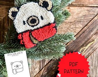 May include: A punch needle craft project featuring a bear face with cream-coloured fur, black ears, and a black nose, wearing a bright red scarf. A white card displays the text PUNCH NEEDLE TEMPLATE BY PEWO DESIGN and a line drawing of the bear.