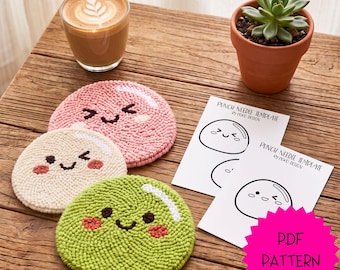 May include: Three round punch needle coasters in pink, cream, and green, each featuring a smiling face with rosy cheeks. Two white paper sheets labeled PUNCH NEEDLE TEMPLATE BY POKO DESIGN are included, along with a pink starburst graphic reading PDF PATTERN.