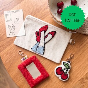 Puede incluir: Una colección de artículos hechos a mano, que incluyen una bolsa de lona con un diseño de zapato rojo, un espejo con marco rojo y un llavero de cereza. Se ve un patrón PDF. Los artículos están dispuestos sobre una superficie de madera.