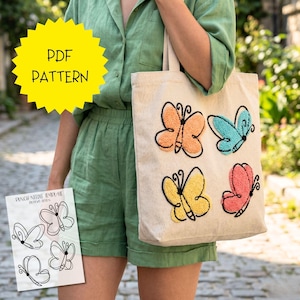 May include: A beige tote bag with four embroidered butterflies in orange, blue, yellow, and pink. The butterflies have black outlines and are on a natural canvas bag. A yellow starburst graphic says "PDF PATTERN".