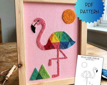 May include: A punch needle embroidery project in a light wood frame featuring a pink flamingo with a multicoloured geometric wing, a textured orange sun, and green triangular hills on a pink fabric background, with a PDF pattern document.