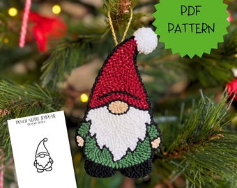 May include: A punch needle gnome ornament featuring a red hat with a white pom-pom, a white beard, and a green body with black boots. A white card displays the text PUNCH NEEDLE TEMPLATE BY DEVO DESIGN and a black line drawing of the gnome.