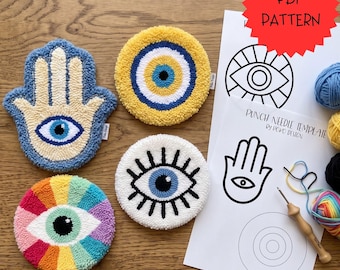 May include: Four punch needle coasters featuring a blue hamsa hand, a yellow eye, a rainbow eye, and a white eye with black lashes. Includes a PDF pattern with a punch needle template by Poko Design, a wooden punch needle tool, and colourful yarn.