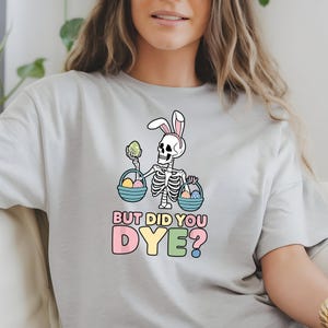 May include: A gray t-shirt with a skeleton wearing bunny ears and holding baskets of Easter eggs. The text on the shirt reads "But did you dye?"