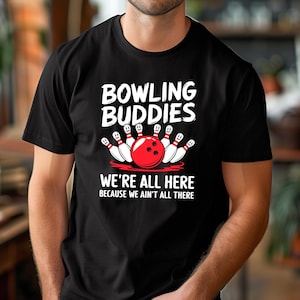 May include: Black t-shirt with a white graphic of bowling pins and a bowling ball. The text "Bowling Buddies" and "We're all here because we ain't all there" is printed on the shirt.