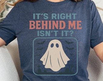 May include: A navy blue t-shirt with the text "IT'S RIGHT BEHIND ME ISN'T IT?" in red and blue. A beige ghost graphic is centered below the text, with bats and a tree line in a square. The shirt is part of a Halloween collection.