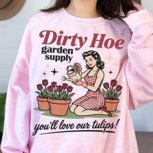 May include: Light pink sweatshirt with the text "Dirty Hoe garden supply" and a vintage illustration of a woman watering tulips. The phrase "you'll love our tulips!" is written below the illustration.