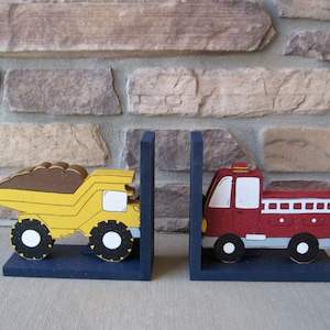 May include: A pair of wooden bookends featuring a yellow dump truck and a red fire truck. The bookends are painted with details and have a blue base.