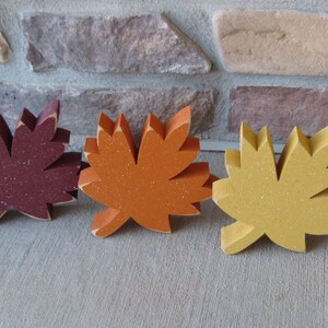 K&ouml;nnte beinhalten: Drei h&ouml;lzerne Herbstbl&auml;tter in verschiedenen Farben. Die Bl&auml;tter sind burgunderrot, orange und gelb. Sie sind alle gleich gro&szlig; und haben die gleiche Form.