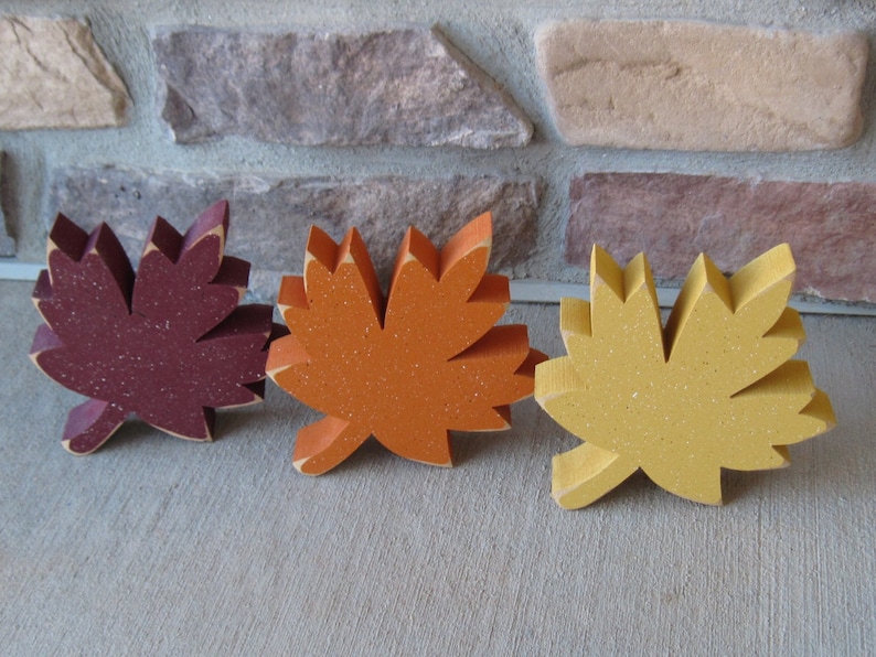 K&ouml;nnte beinhalten: Drei h&ouml;lzerne Herbstbl&auml;tter in verschiedenen Farben. Die Bl&auml;tter sind burgunderrot, orange und gelb. Sie sind alle gleich gro&szlig; und haben die gleiche Form.