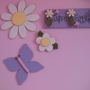 May include: Purple butterfly, white daisy with yellow centre, and a sign that reads "Dance Giggle" with pink butterflies on a pink background.