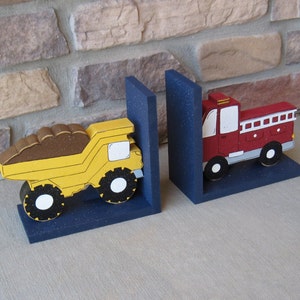 May include: A pair of wooden bookends featuring a yellow dump truck and a red fire truck. The bookends are painted with details and have a blue base.