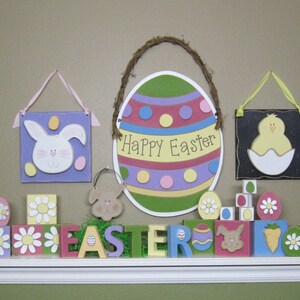 May include: A colorful Easter decoration with a large egg-shaped sign that says "Happy Easter" and a variety of wooden blocks with Easter-themed designs, including bunnies, chicks, and flowers.