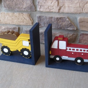 May include: A pair of bookends featuring a yellow dump truck and a red fire truck. The bookends are made of wood and painted in bright colors. They are a fun and whimsical way to add a touch of personality to any bookshelf.