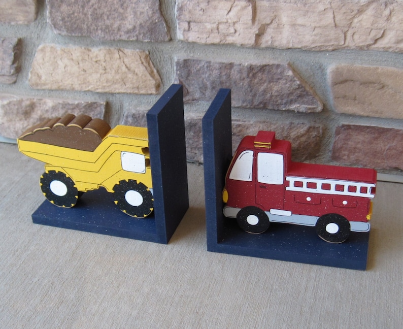 May include: A pair of bookends featuring a yellow dump truck and a red fire truck. The bookends are made of wood and painted in bright colors. They are a fun and whimsical way to add a touch of personality to any bookshelf.